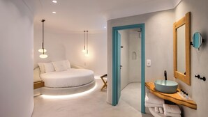 Un dormitorio moderno con cama redonda, lámparas de noche y un tocador de madera con lavabo.