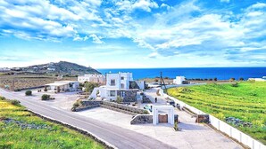 Una propiedad costera con camino de entrada pavimentado que conduce a un edificio blanco, rodeada de campos verdes y un cielo azul despejado.