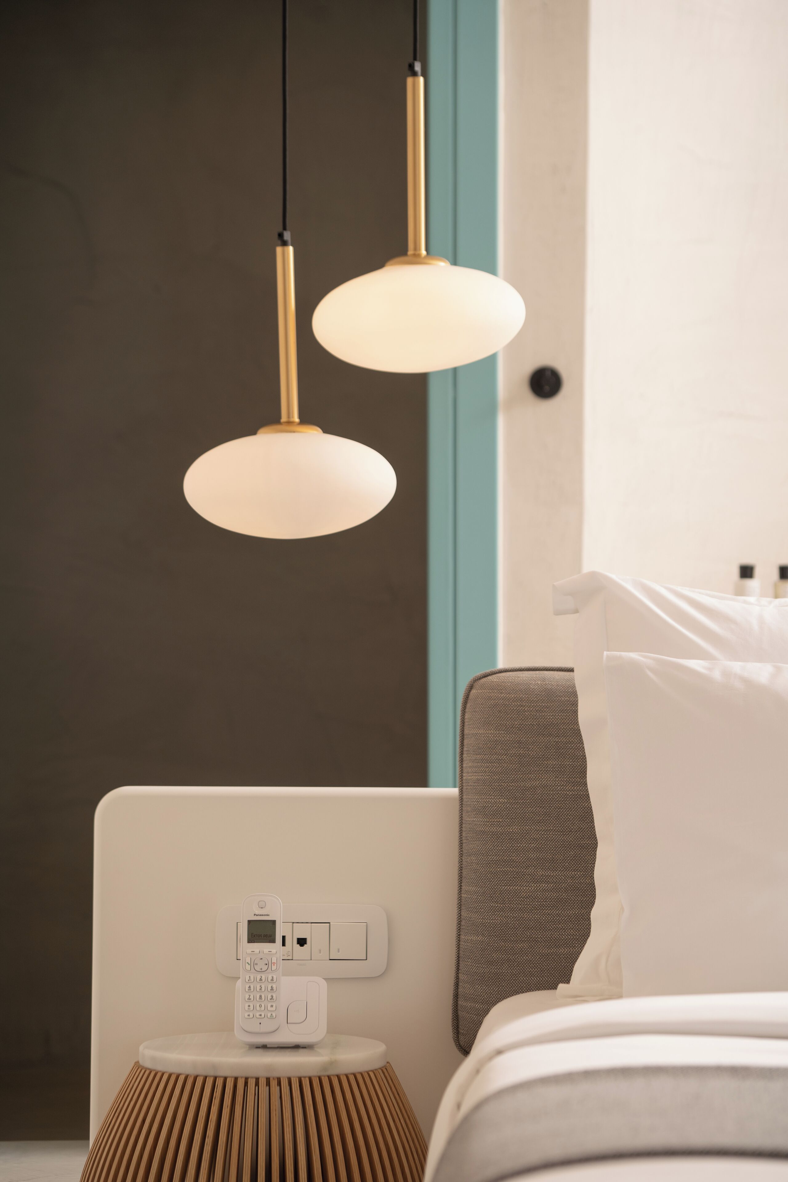 A modern hotel room with a bed, a bedside table with a phone, and two pendant lights.