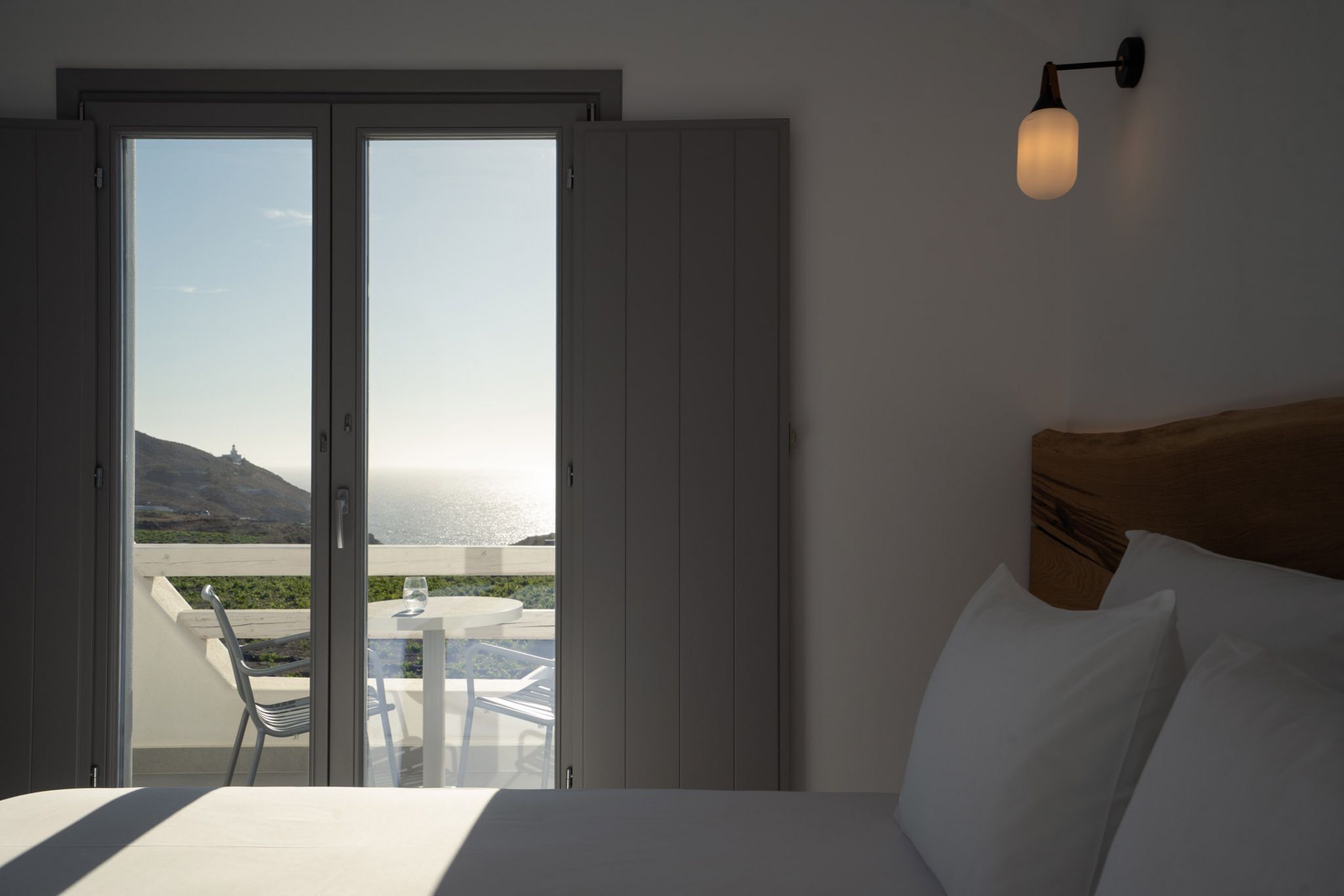 A hotel room with a bed, a nightstand, a table with chairs, and a view of the ocean through a sliding door.