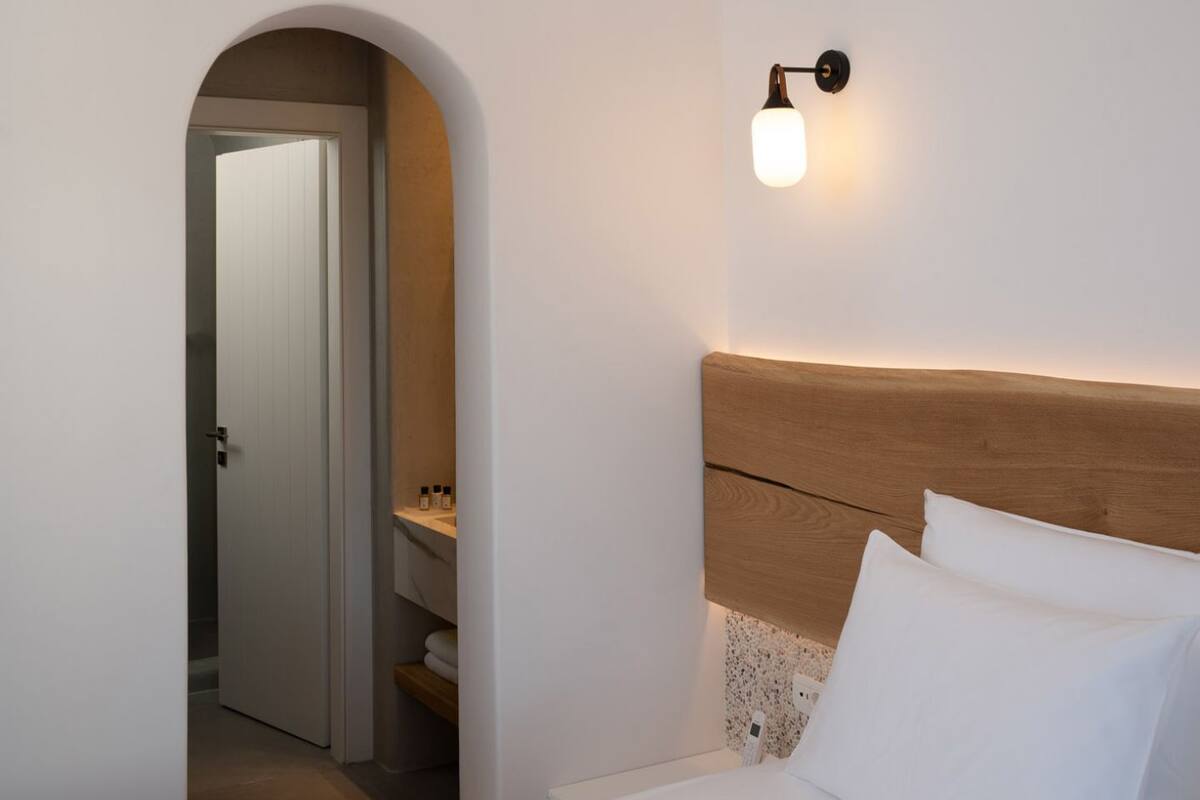 A bedroom with a bed, a nightstand, a wall-mounted light, and an arched doorway leading to another room.