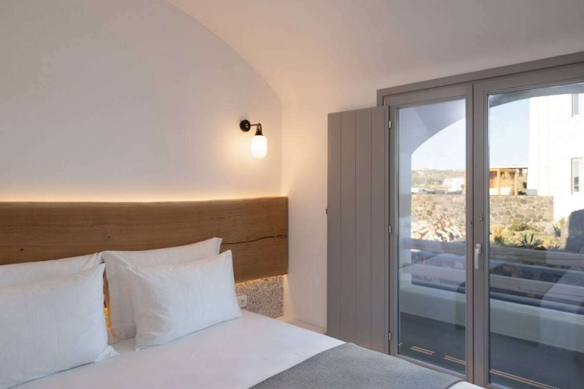 A bedroom with a wooden headboard, white bedding, and a view through a sliding glass door to an outdoor area.