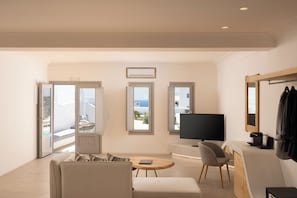 Een moderne woonkamer met een bank, een ronde salontafel, een televisie en een balkon met uitzicht op zee.