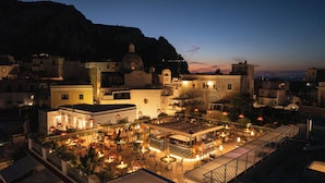 A rooftop bar with outdoor seating, surrounded by buildings with Mediterranean architecture, under a twilight sky. - Hotel La Palma, Oetker Hotels (Capri)