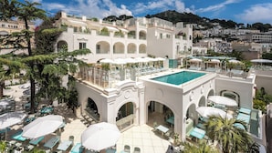 A rooftop pool area with multiple lounge chairs and umbrellas, surrounded by white buildings with balconies and greenery. - Hotel La Palma, Oetker Hotels (Capri)