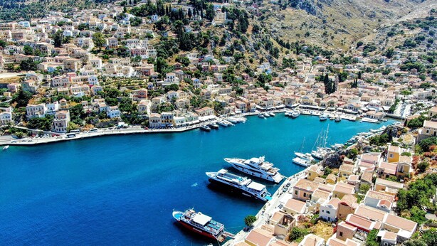 A coastal town with a marina, featuring numerous boats and yachts docked. - Marikas Deluxe Rooms (Symi)