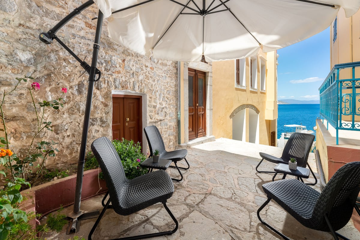 A stone building with a balcony, outdoor seating, and a view of the sea.