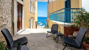 A balcony with wicker chairs, a view of the sea, and a stone-paved floor. - Marikas Deluxe Rooms (Symi)