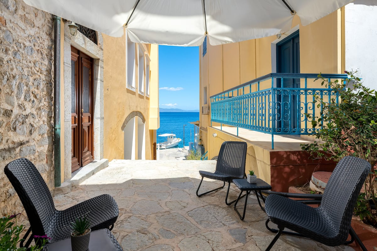 A balcony with wicker chairs, a view of the sea, and a stone-paved floor.