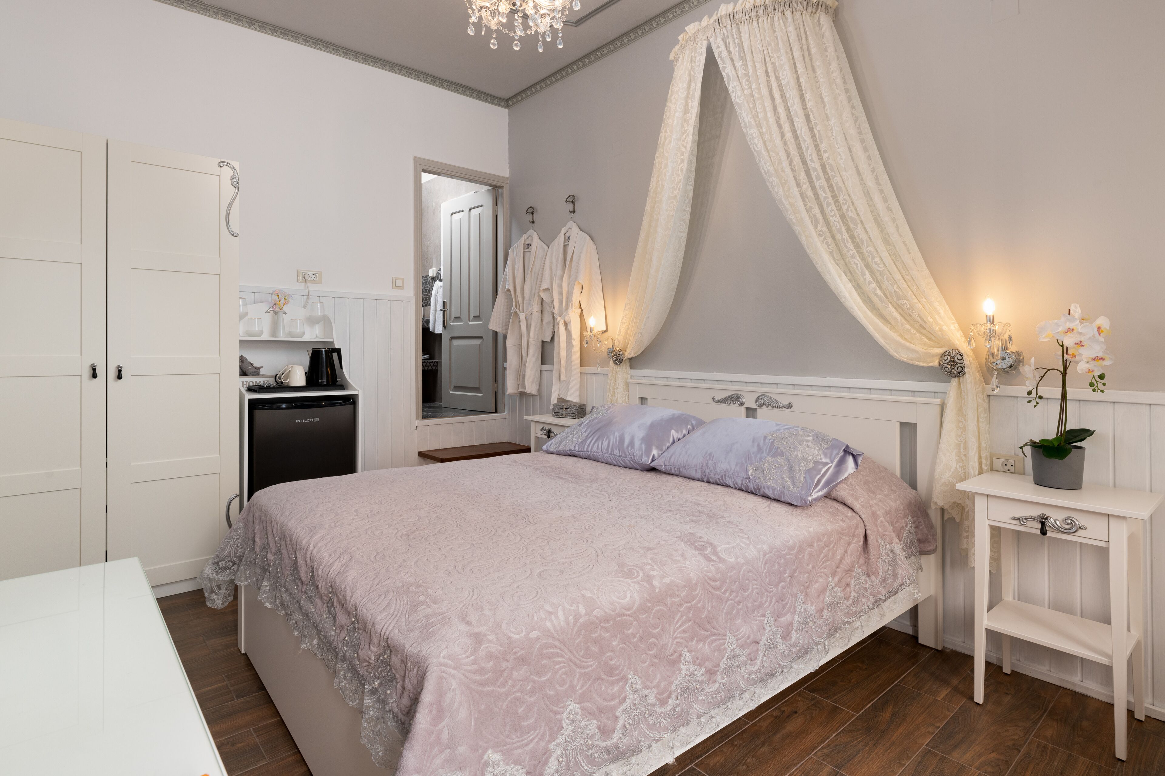 A bedroom with a bed, bedside tables, a mirror, a wardrobe, and a chandelier.