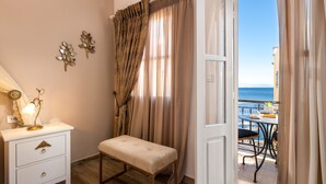 A room with a bench, a bedside table with a lamp, and a view of the sea through a balcony. - Marikas Deluxe Rooms (Symi)