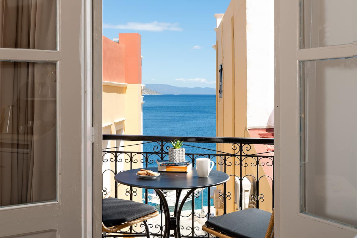 A balcony with a view of the sea, a small table with a plant, a book, and a mug.