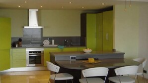 Una cucina moderna con mobili verdi, un'isola centrale con sedie e un forno a incasso.