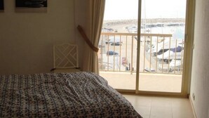 Una camera da letto con un letto, una finestra che si affaccia su un porto turistico e una porta che dà su un balcone.