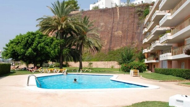 Una piscina con una persona che nuota, circondata da palme e un edificio con balconi.