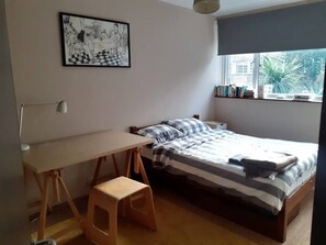 Ein Schlafzimmer mit Bett, Schreibtisch, Stuhl und Fensterbank mit Büchern.