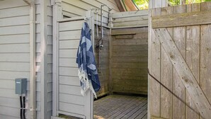 Een buitendouche van hout met een metalen deur, een handdoek aan een rek en een houten terras.