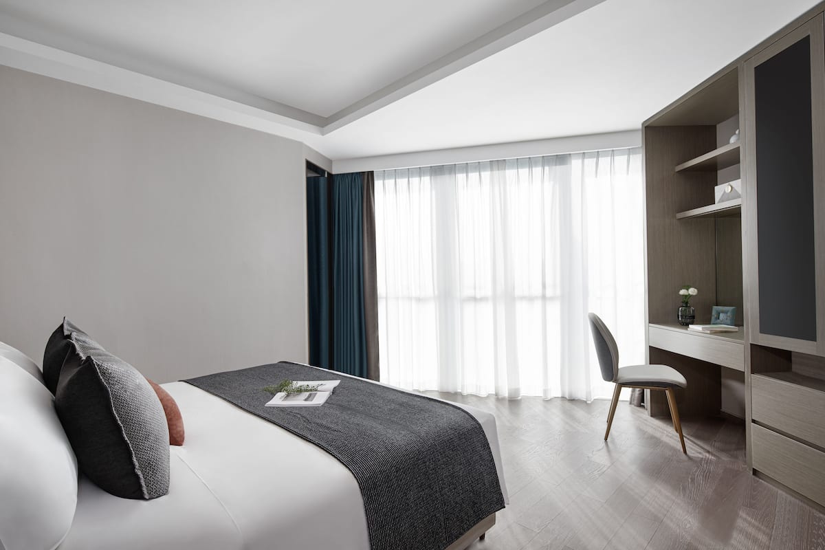 A modern hotel room with a large bed, a desk, and a wardrobe.