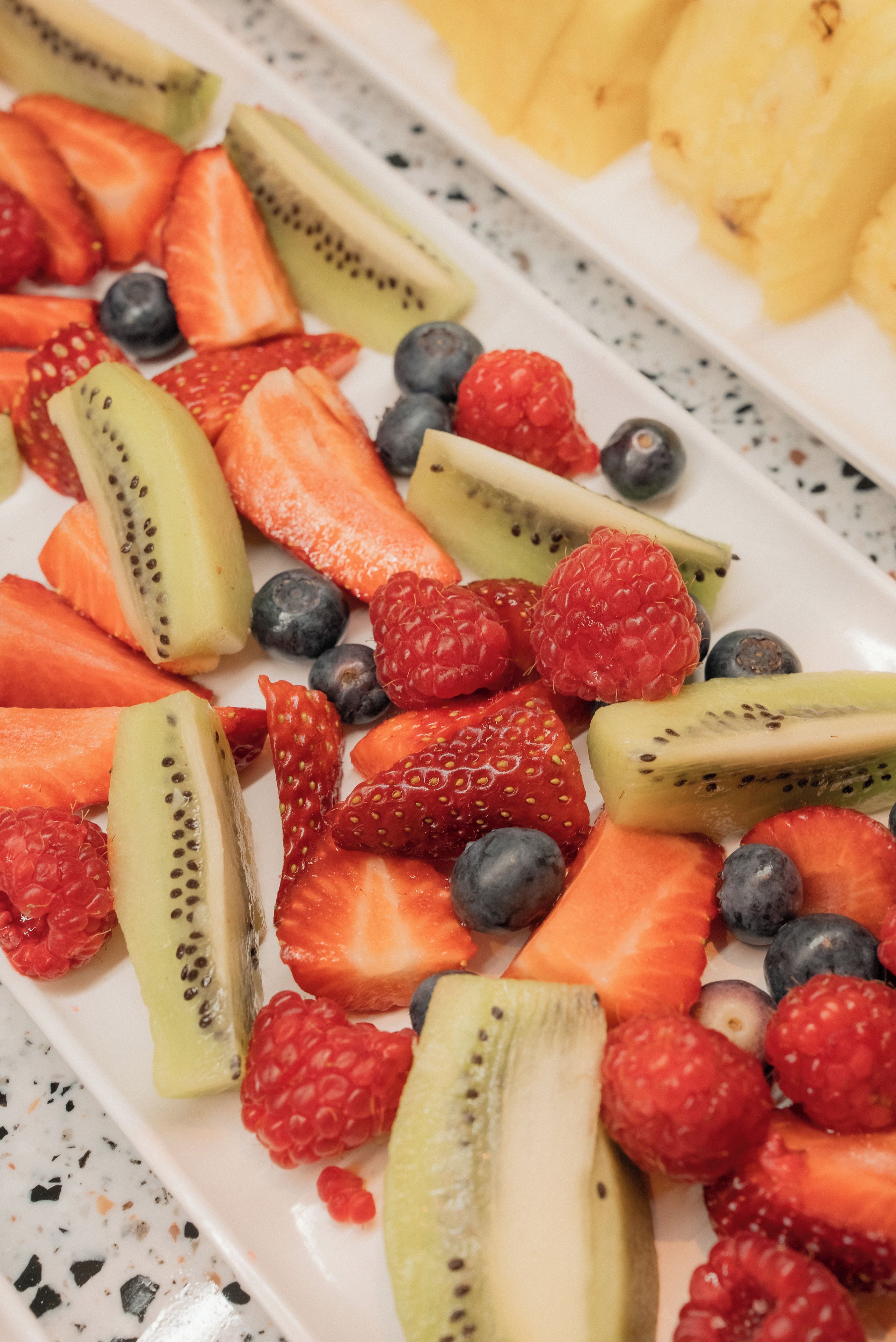 Un plato blanco con frutas cortadas, incluyendo fresas, kiwi, frambuesas y arándanos.