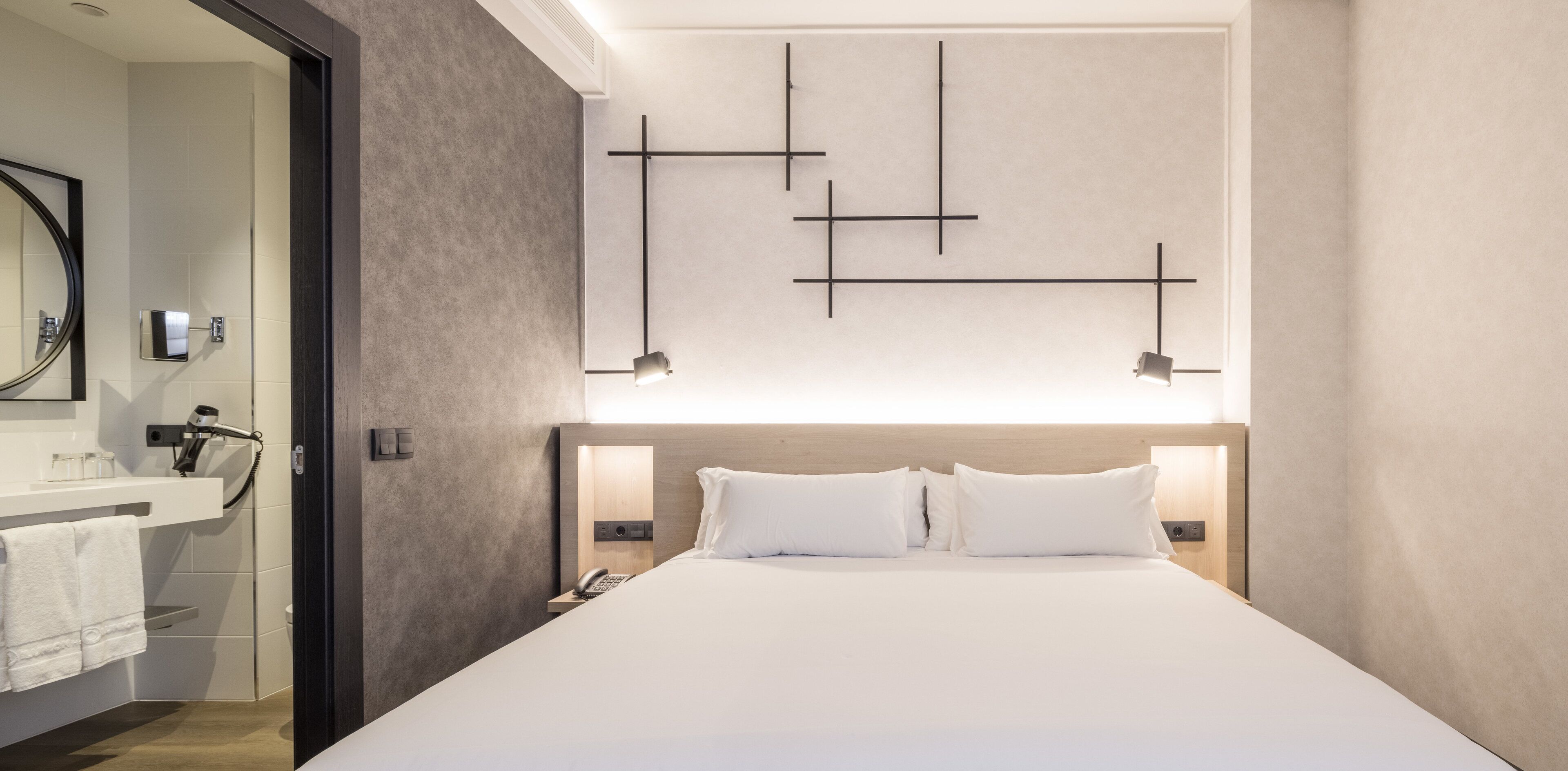 Une chambre d’hôtel moderne dotée d’un grand lit, d’un bureau intégré, d’un miroir et d’un luminaire fixé au mur.
