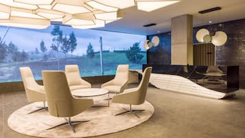 A modern interior with a large window, a round table with four chairs, and a unique ceiling light fixture.