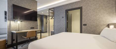 Una habitación de hotel moderna con una cama grande, un escritorio con silla, un televisor de pantalla plana en la pared y un vestidor.