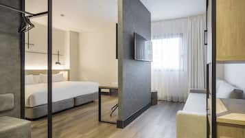 A modern hotel room with a large bed, a desk, a TV, and a sofa.