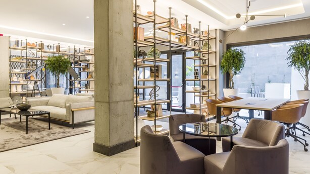 Un interior moderno con sofá, mesa de centro, sillas, una amplia estantería y una zona de comedor con mesa y sillas.