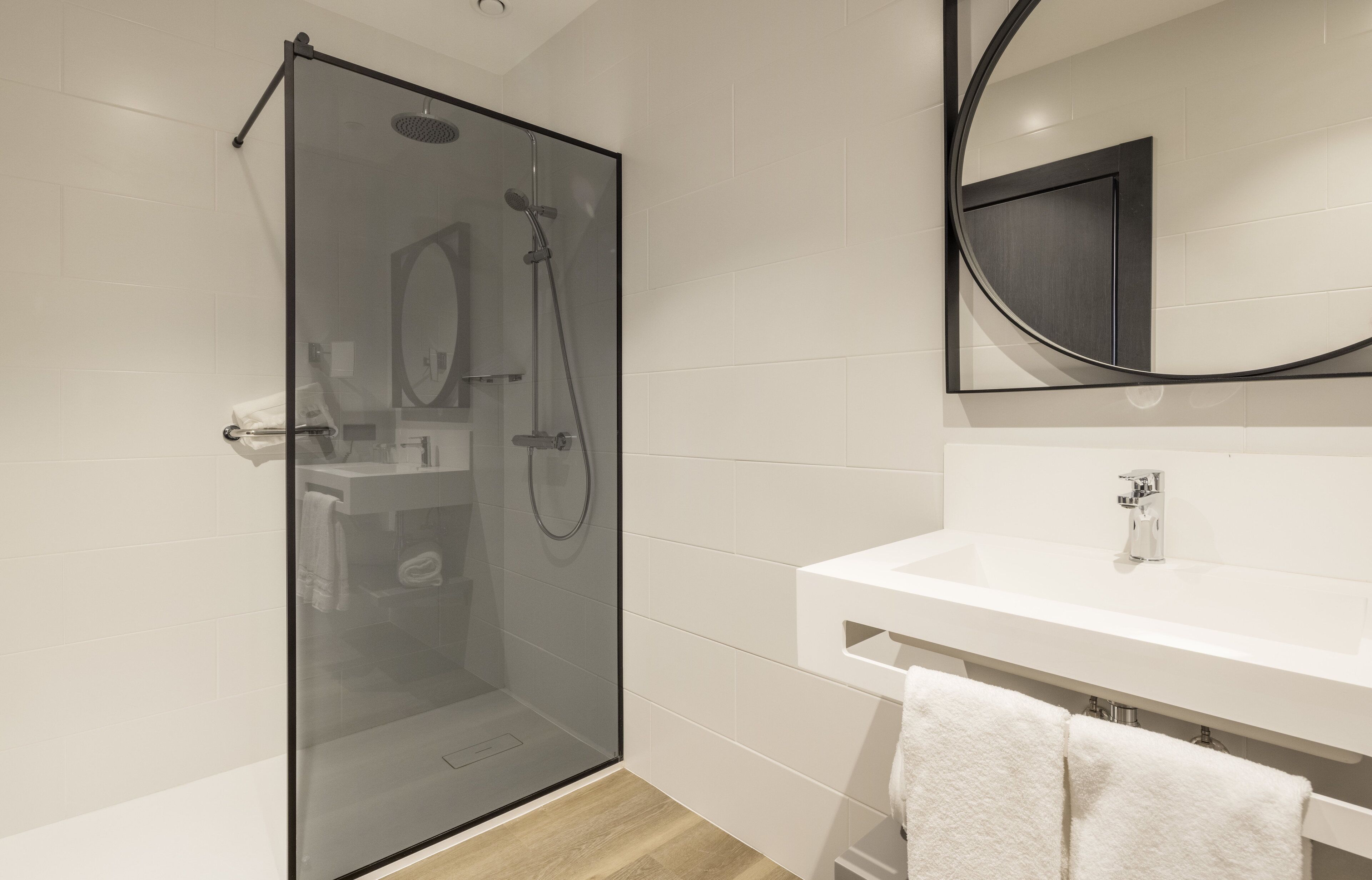 A modern bathroom with a glass-enclosed shower, a white sink, and a mirror with a black frame.