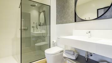 A modern bathroom with a glass-enclosed shower, a white toilet, and a vanity with a mirror and sink.