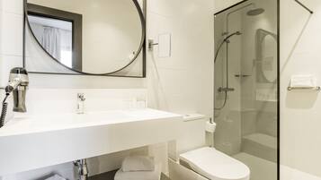 Un baño moderno con lavamanos blanco, espejo, inodoro y ducha con mampara de vidrio.