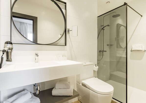 Un baño moderno con lavamanos blanco, espejo, inodoro y ducha con mampara de vidrio.