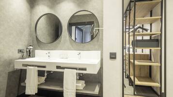 Une salle de bain moderne avec un grand miroir, deux petits miroirs ronds, un lavabo blanc et un porte-serviettes.