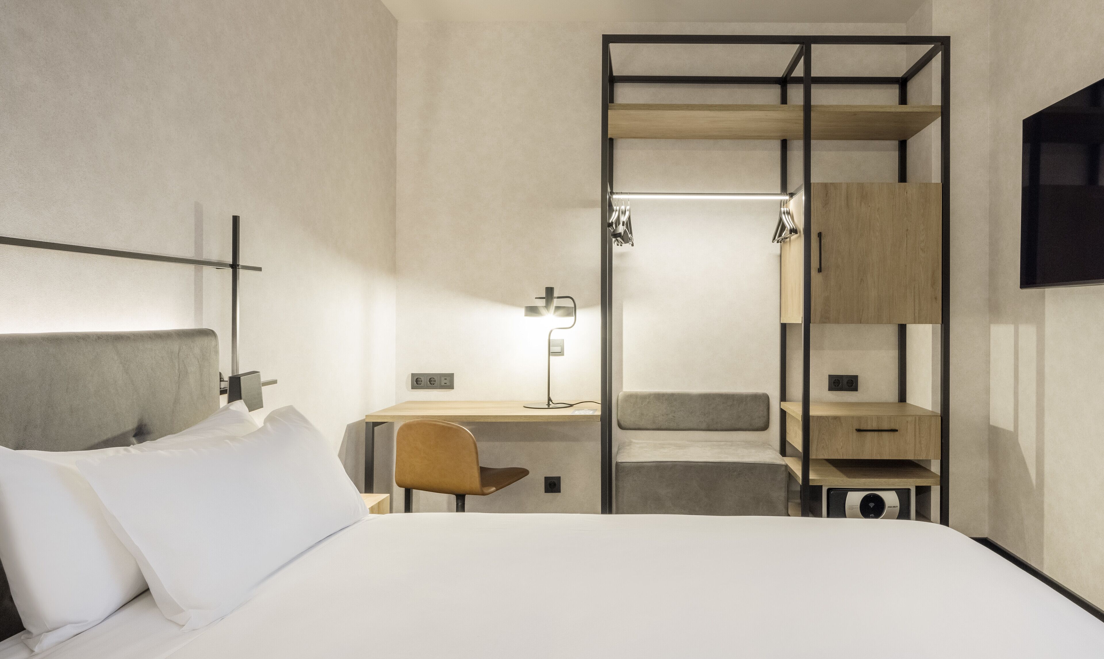 Una habitación de hotel moderna con cama, escritorio, silla, armario y televisión.