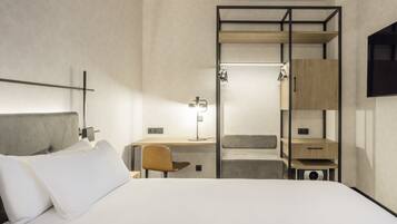 A modern hotel room with a bed, a desk, a chair, a wardrobe, and a TV.
