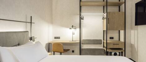 Una habitación de hotel moderna con cama, escritorio, silla, armario y televisión.