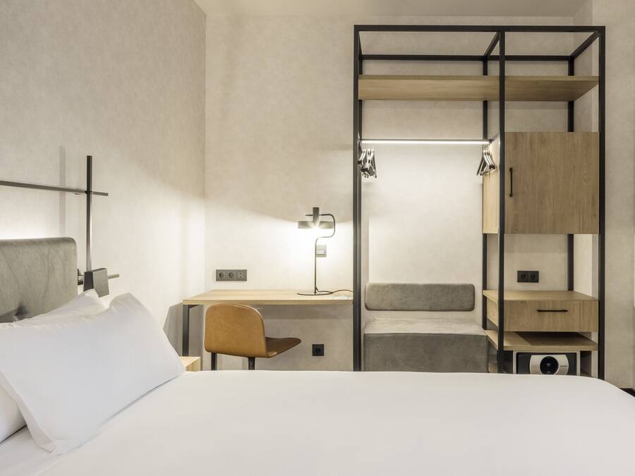 A modern hotel room with a bed, a desk, a chair, a wardrobe, and a TV.