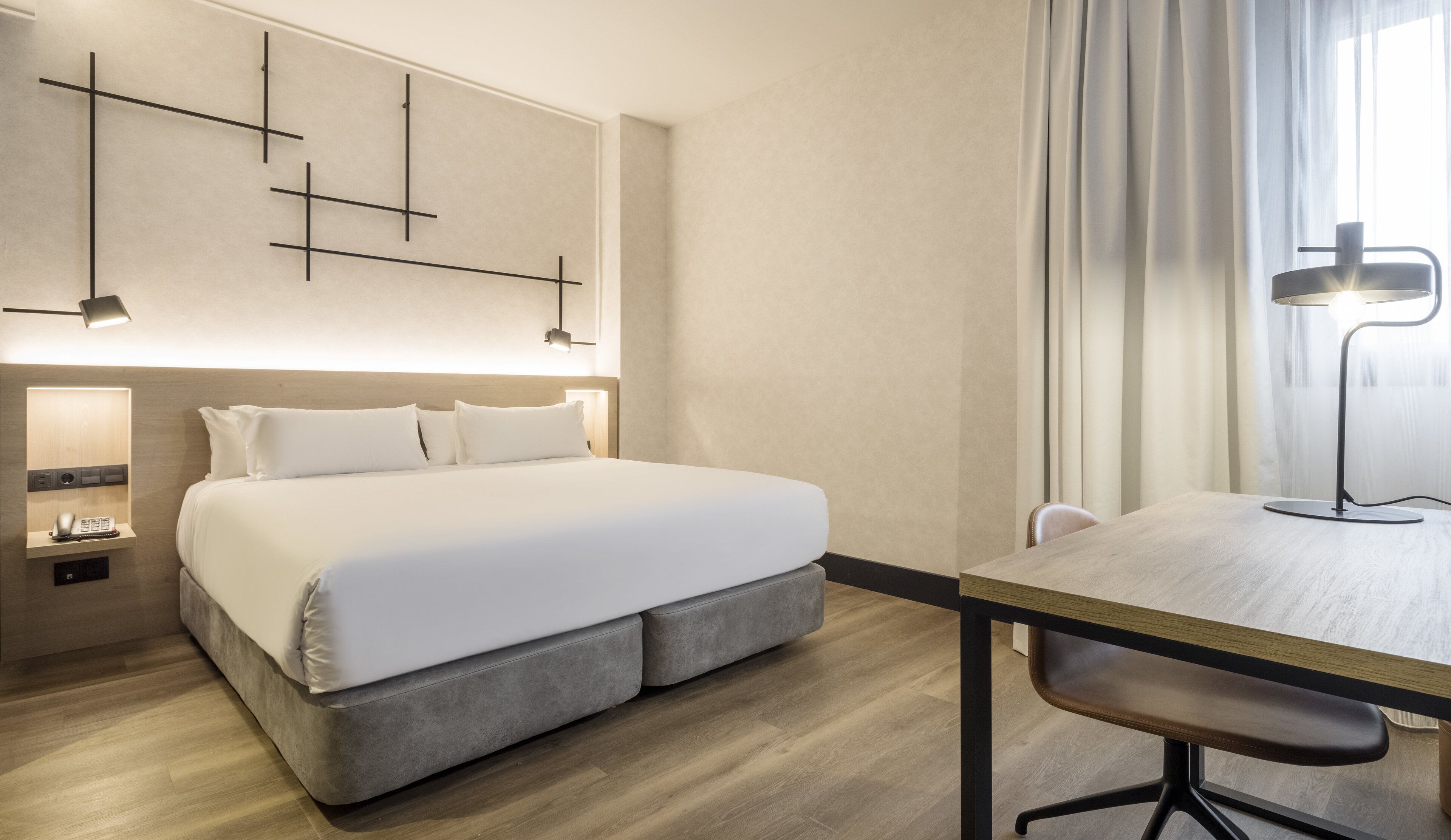 Ett hotellrum med en stor säng, sängbord, ett skrivbord med en stol och en modern väggdesign.