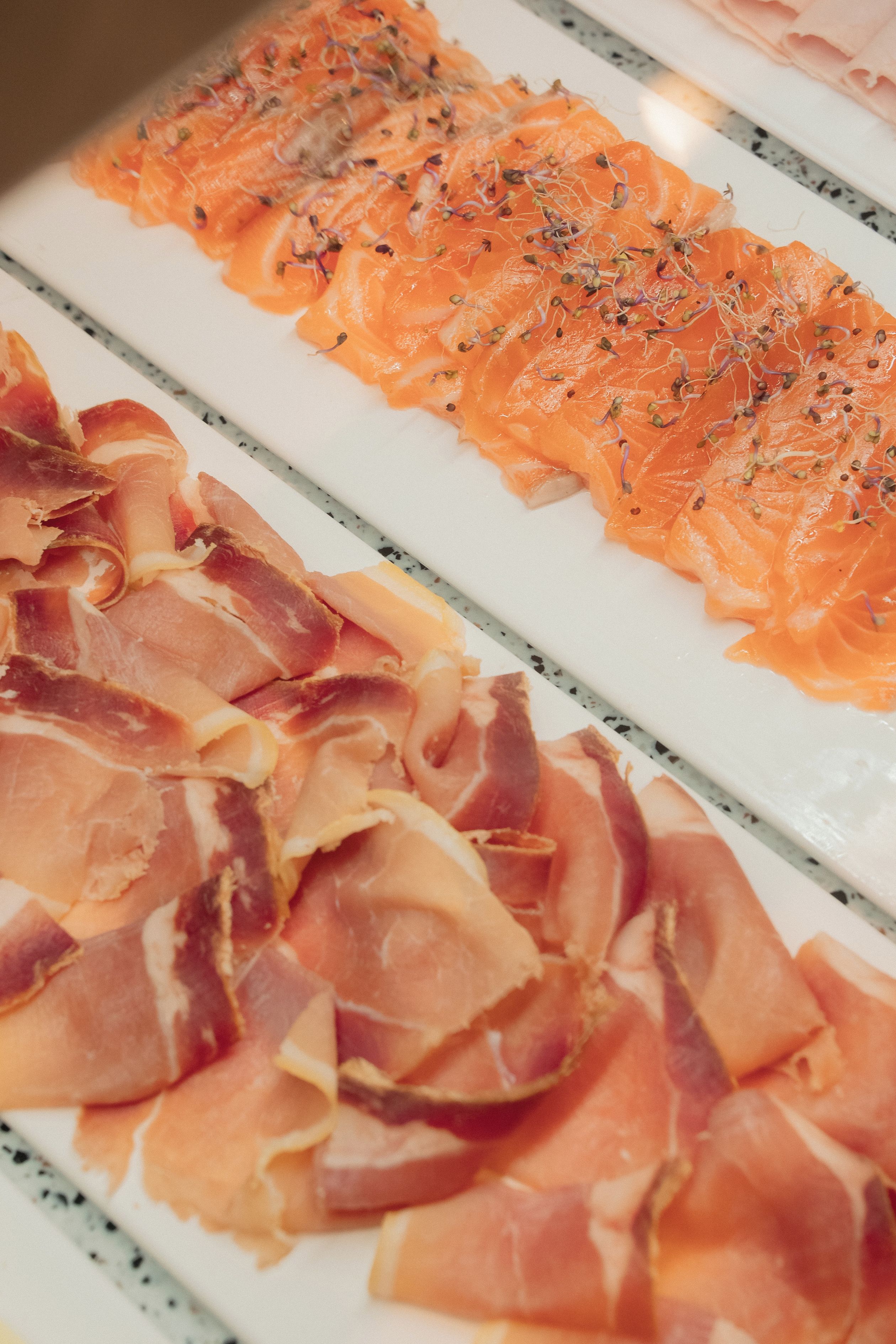A variety of cured meats, including prosciutto and salami, displayed on a white surface.