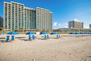 Un hotel frente a la playa con varios pisos, sillas y sombrillas.