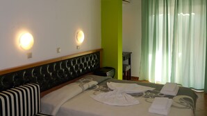 A hotel room with a bed, two wall-mounted lights, a green accent wall, and a window with green curtains.
