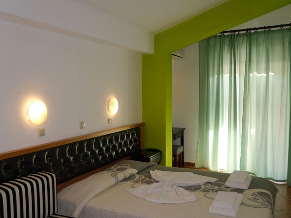 Hotelkamer met een bed, twee wandlampen, een groene accentmuur en een raam met groene gordijnen.
