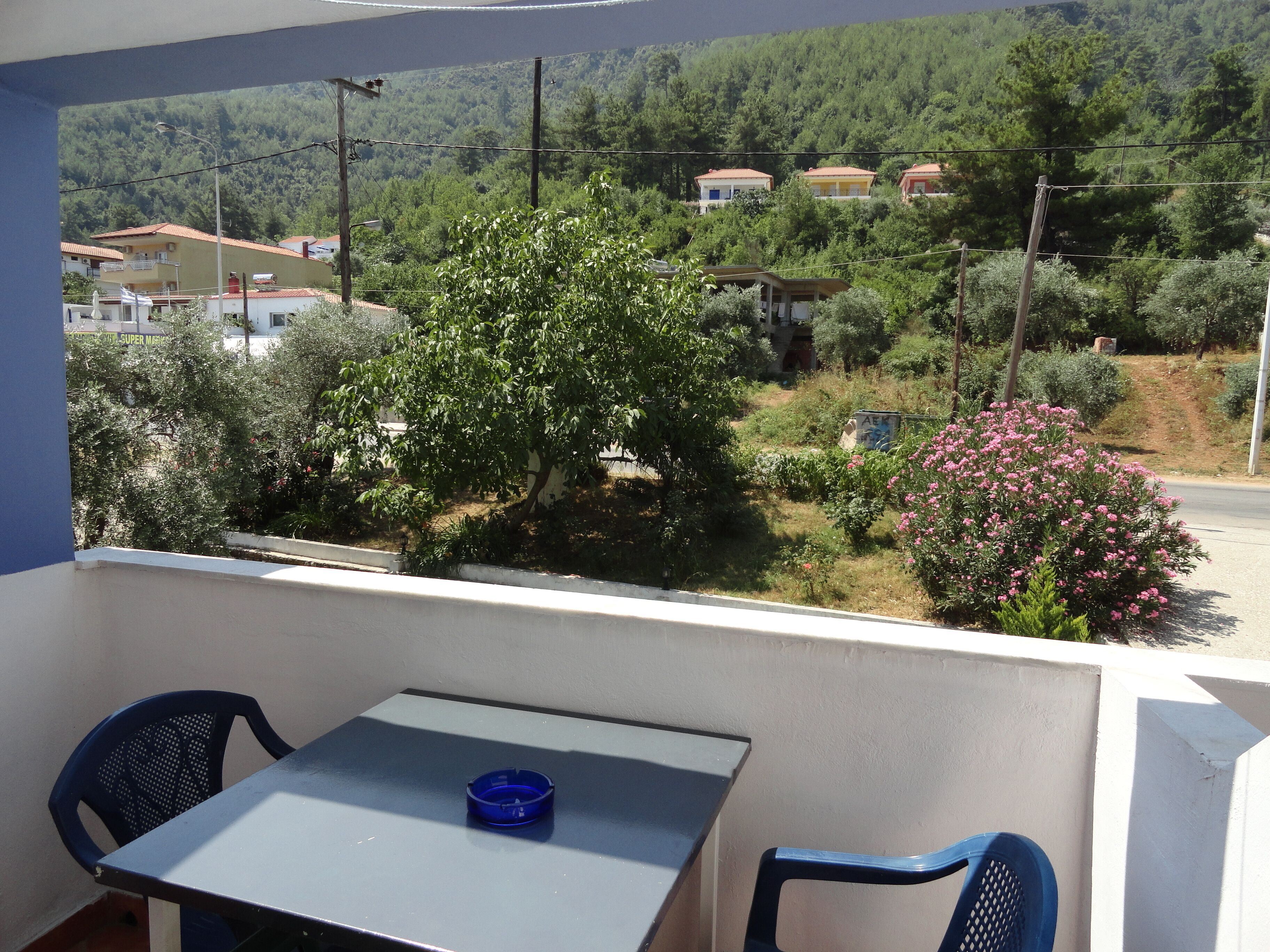 Un balcón con una mesa y sillas, con vista a una colina con casas y vegetación.