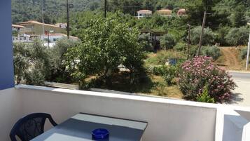 Un balcón con una mesa y sillas, con vista a una colina con casas y vegetación.