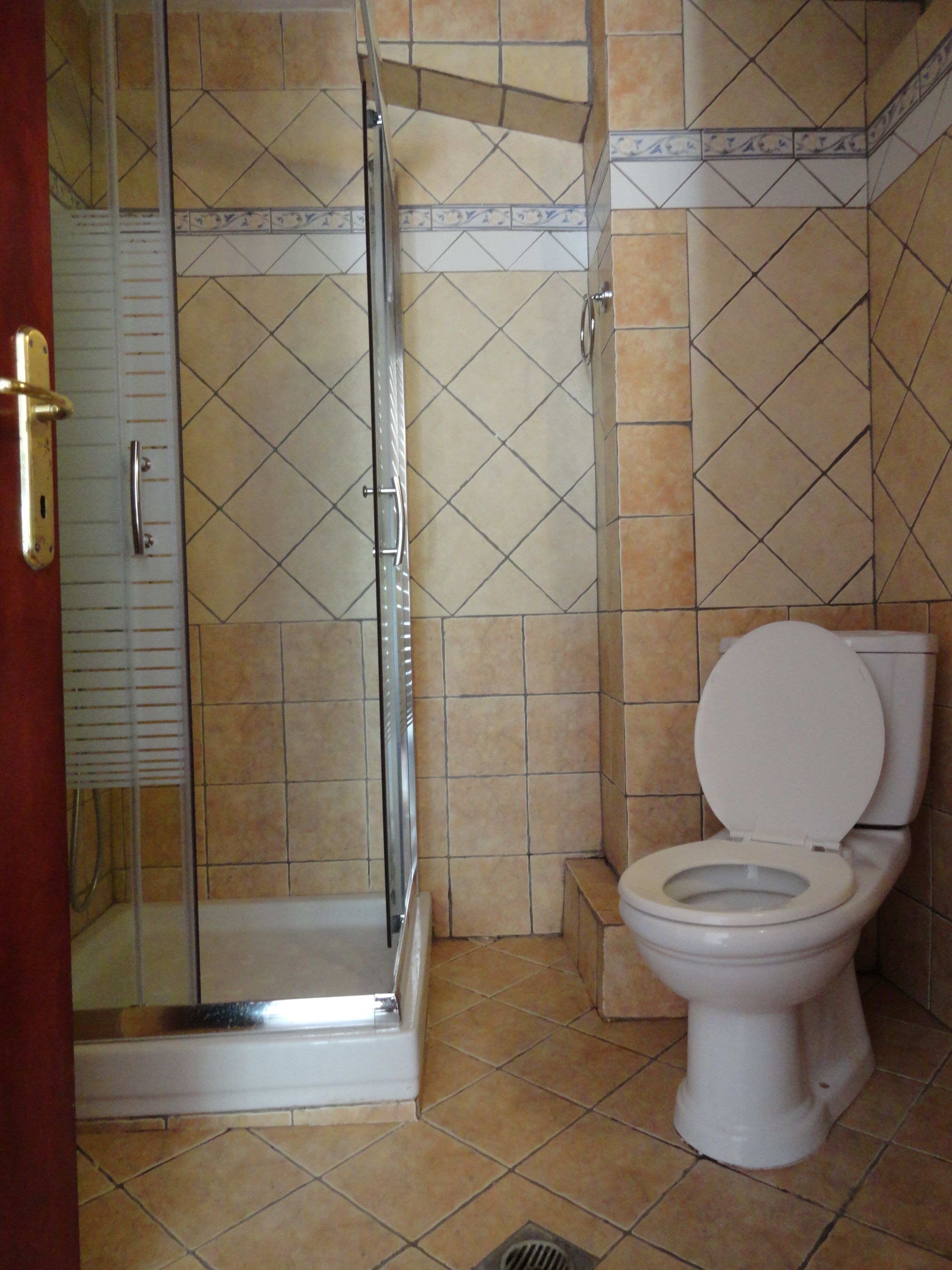 A bathroom with a glass shower enclosure, a toilet, and tiled walls.