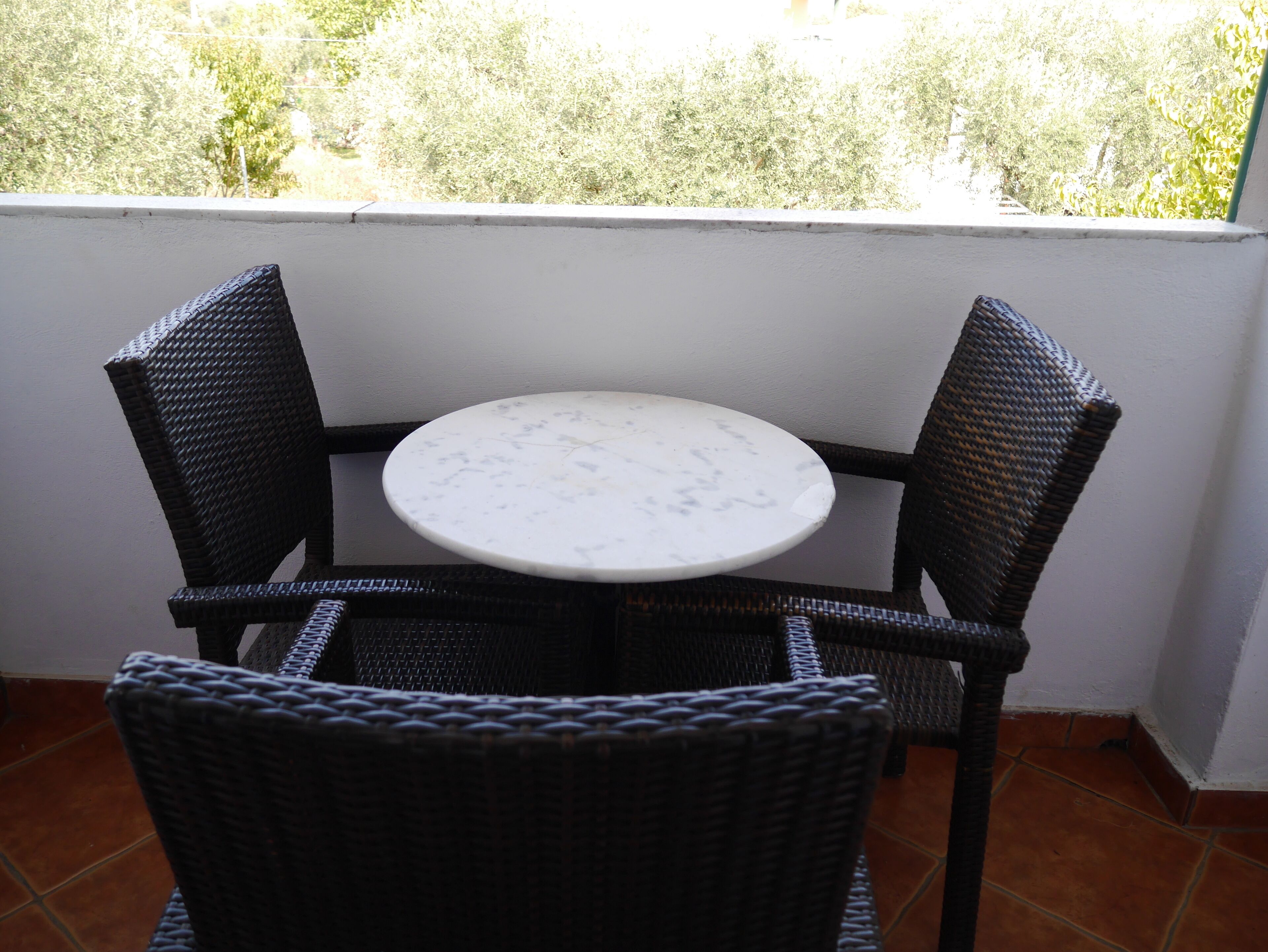 A small round table with a white marble top, surrounded by four wicker chairs.