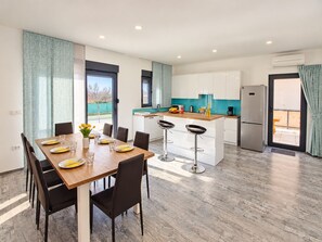 A modern kitchen with a central island, bar stools, and a dining table set for four. - Villa Serenity – Stylish 3-Bedroom Retreat with Private Pool (Vodnjan)