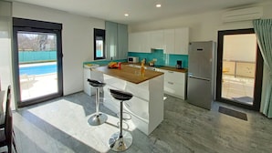 A modern kitchen with a central island, two bar stools, a refrigerator, and a view of a swimming pool. - Brand new villa with private pool on peaceful location (Vodnjan)