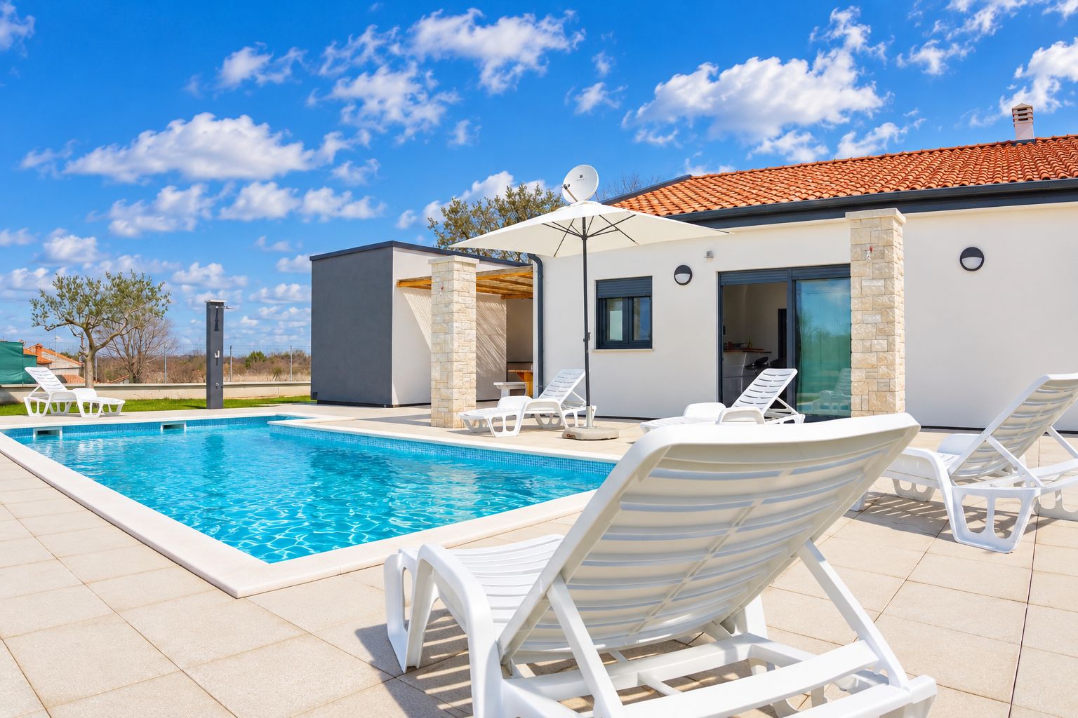 A modern outdoor swimming pool with white lounge chairs and a covered seating area.