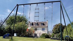Une balançoire installée dans une cour verdoyante, avec une maison en arrière-plan.